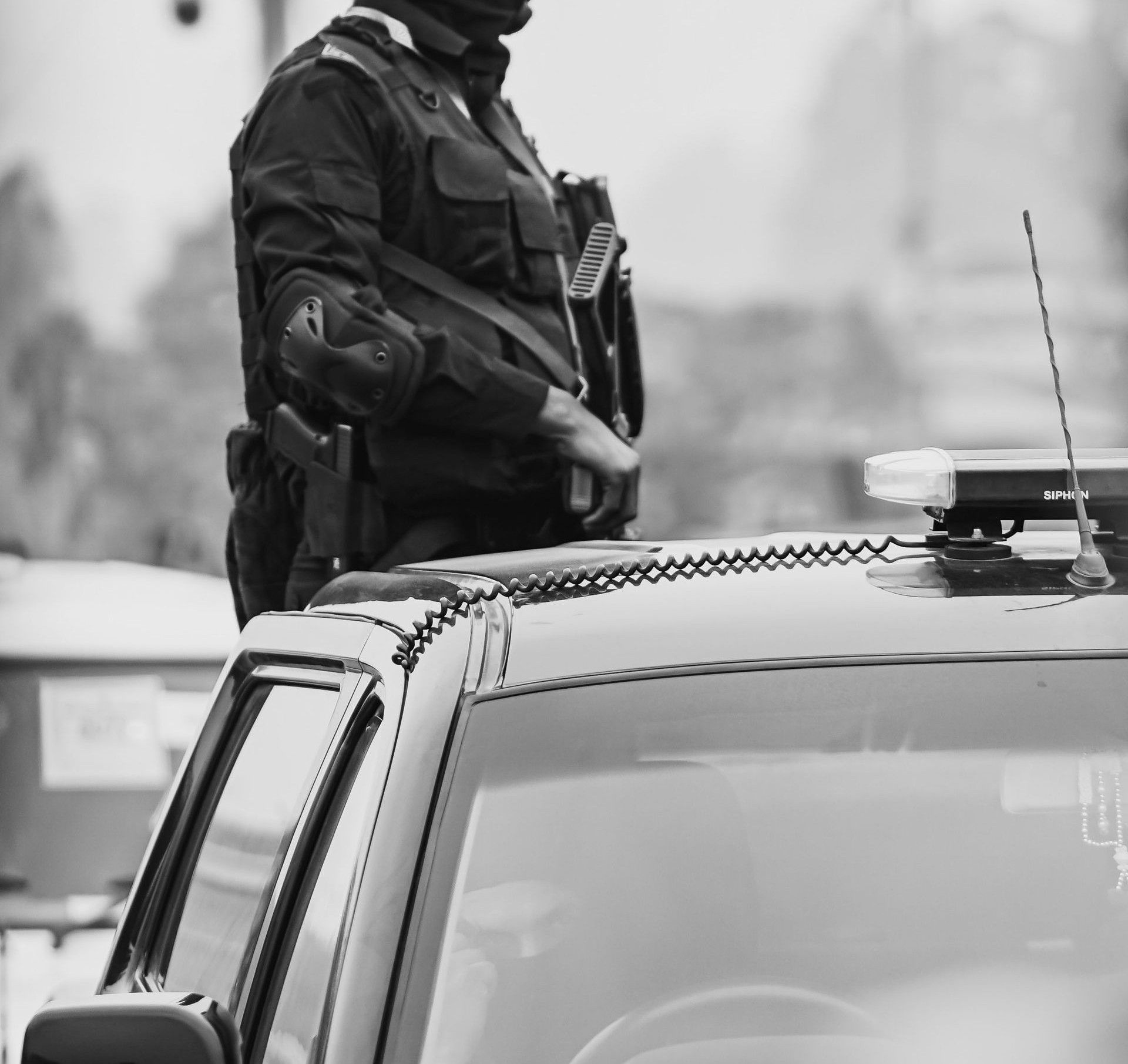 Black and white photo of armed soldier on duty in New Delhi street, standing on a vehicle.