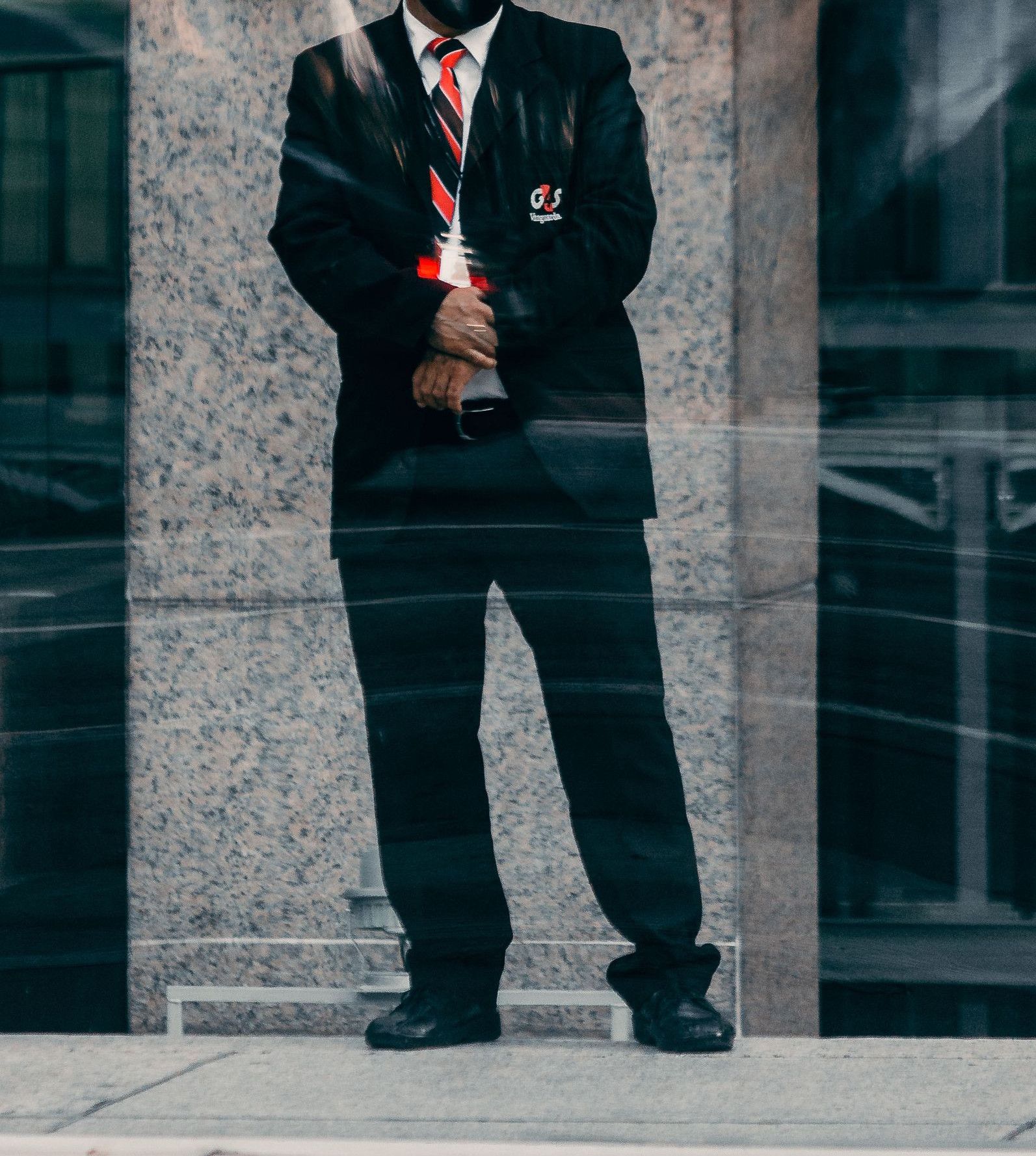 Bald security guard in black suit and tie stands in an urban environment, providing security.