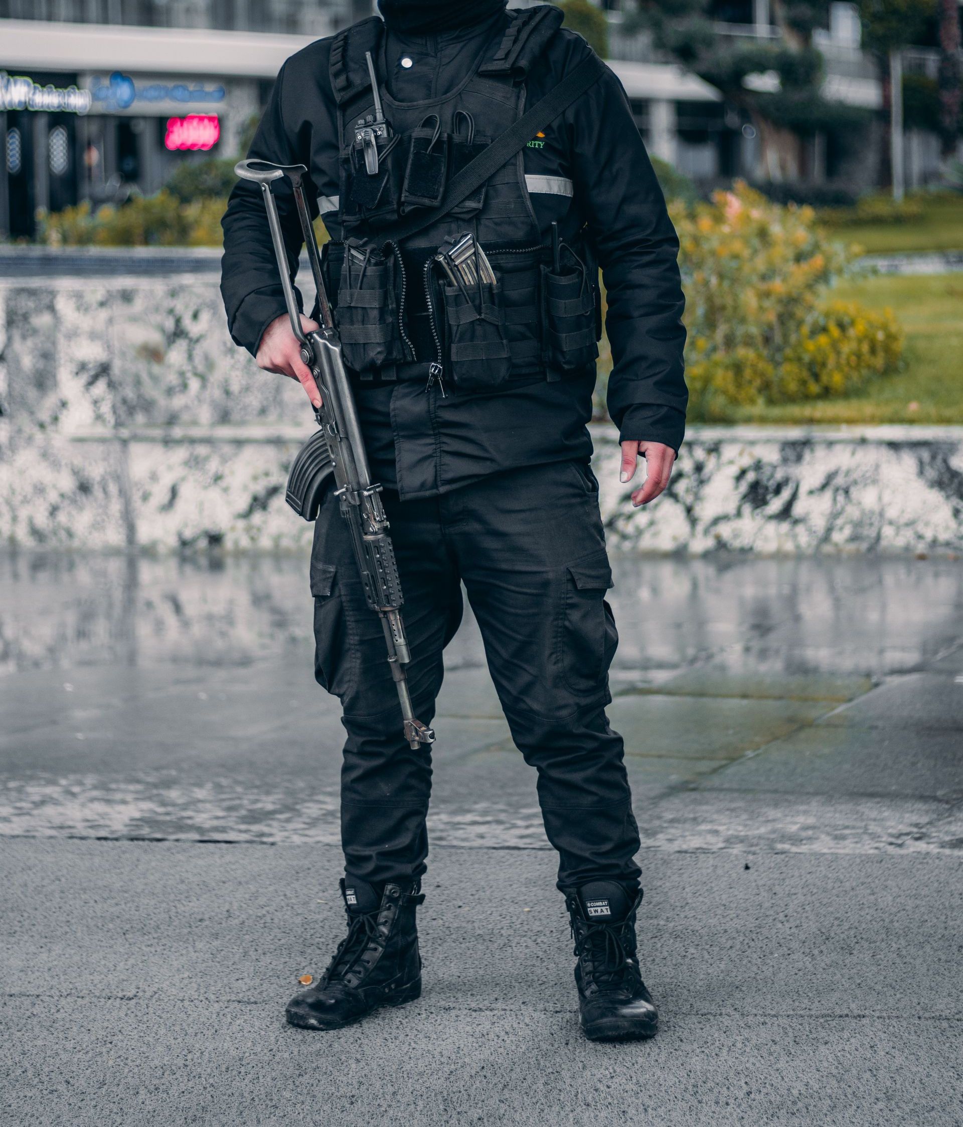 Police officer standing outdoors holding a rifle in an urban area.