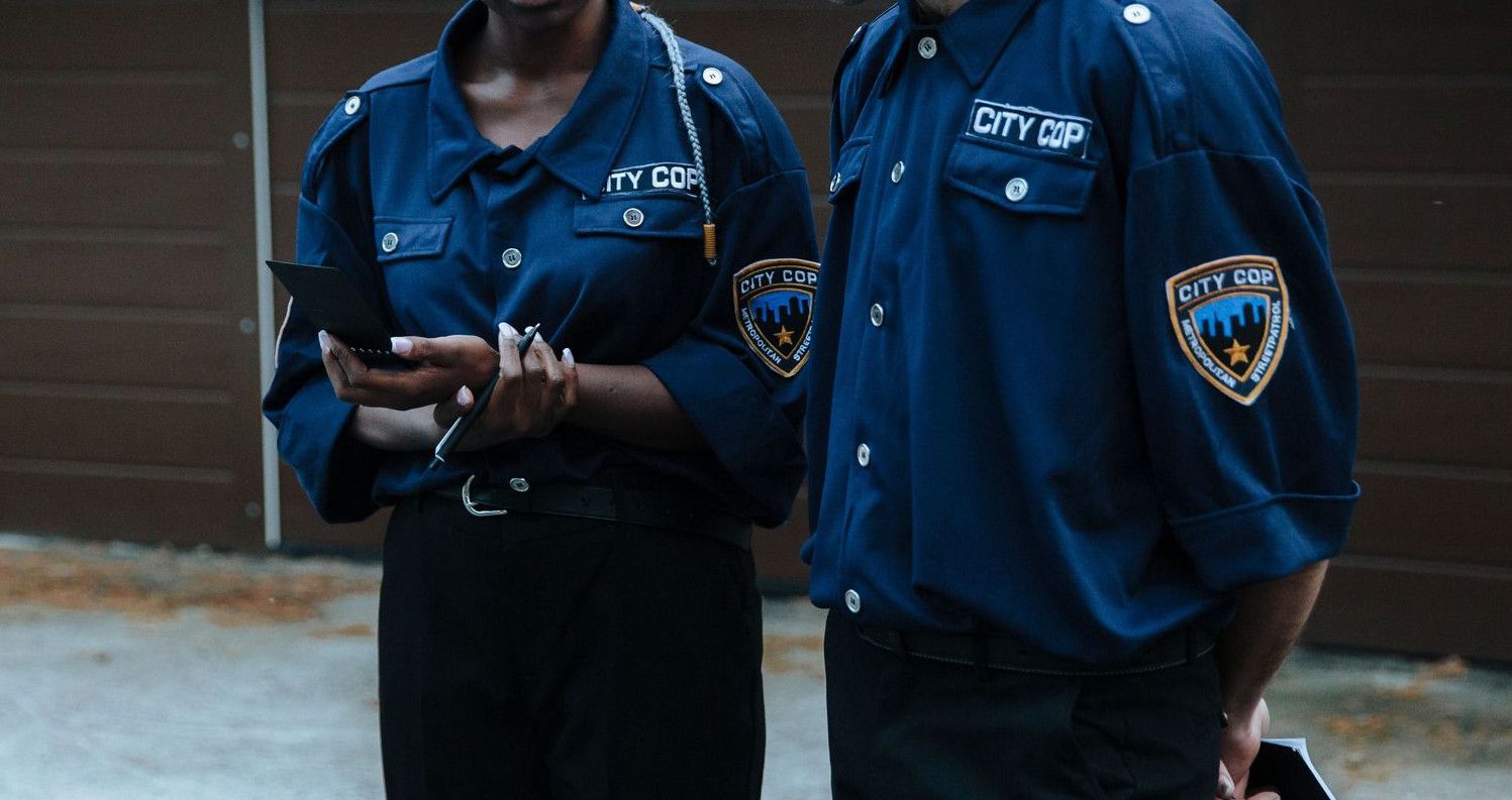 Two police officers in uniform discussing a case outside a residential garage.