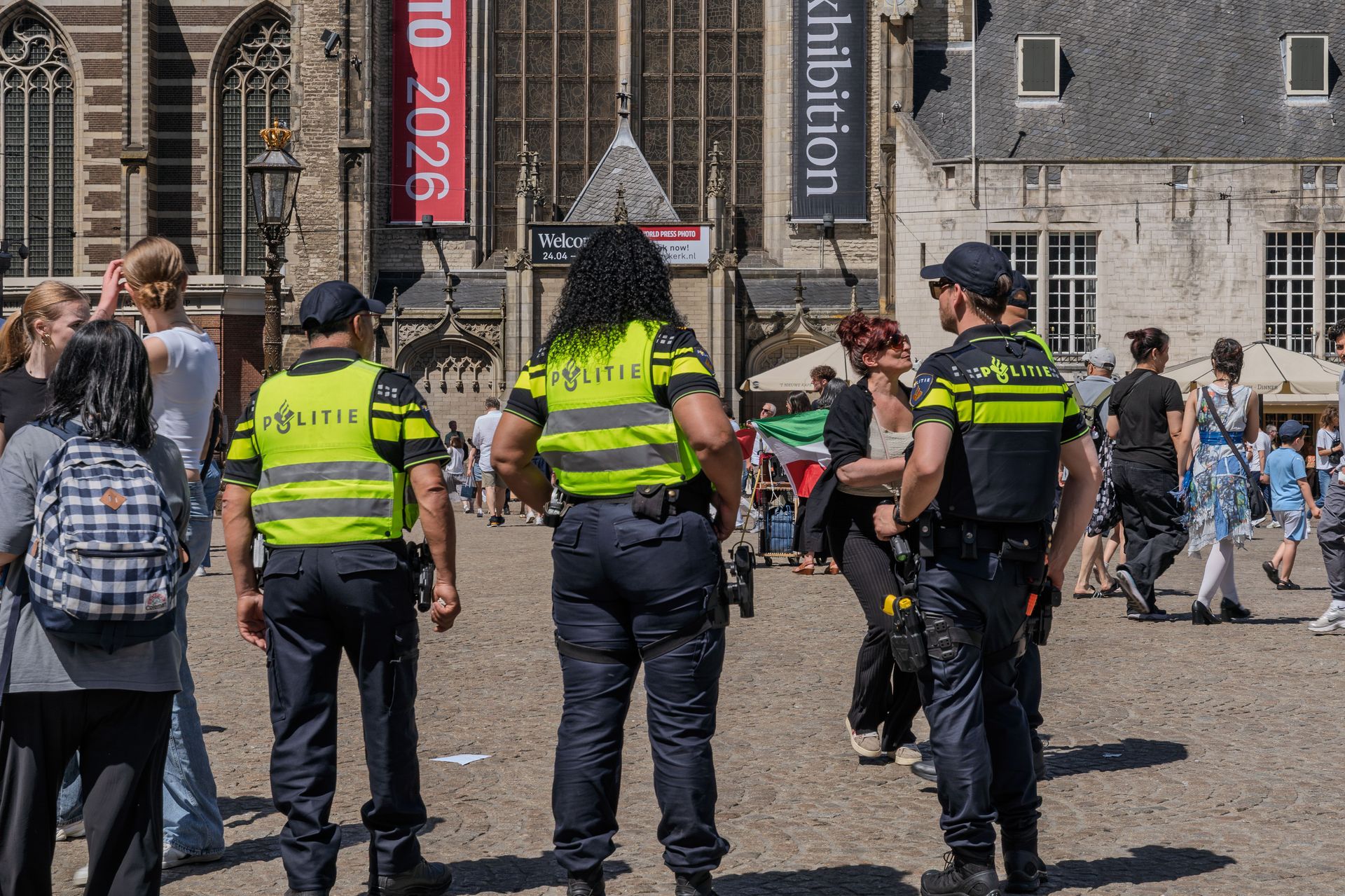 Dutch police officers monitoring a busy square in front of historic buildings in Amsterdam.